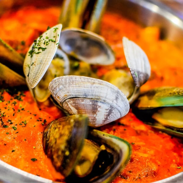 Clams and mussels in a vibrant orange sauce, garnished with herbs, from The Crab Station.