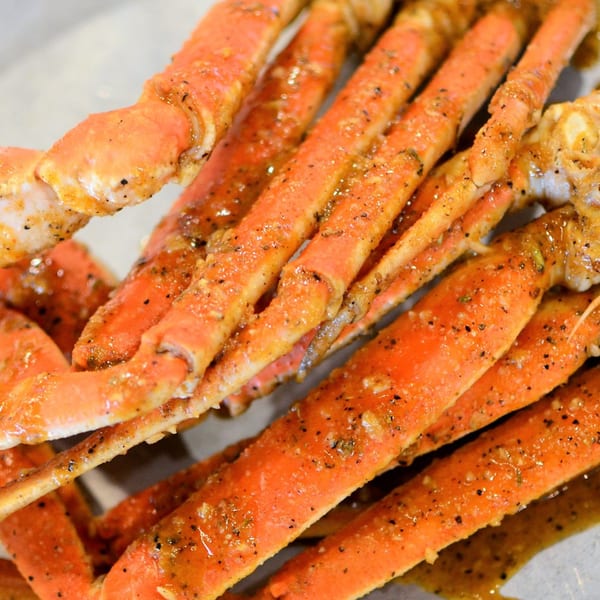 Close-up of several bright orange crab legs, seasoned with black pepper and a savory sauce.