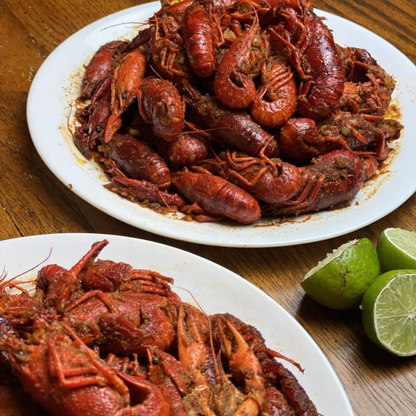 Two plates piled high with seasoned red crawfish, with lime wedges on a wooden table.