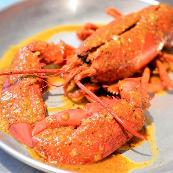 A whole cooked lobster, bright red and covered in a savory sauce, served on a metal platter.