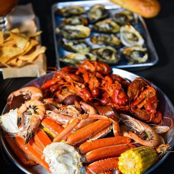 A seafood boil with crab legs, shrimp, crawfish, corn, and oysters on a dark table.
