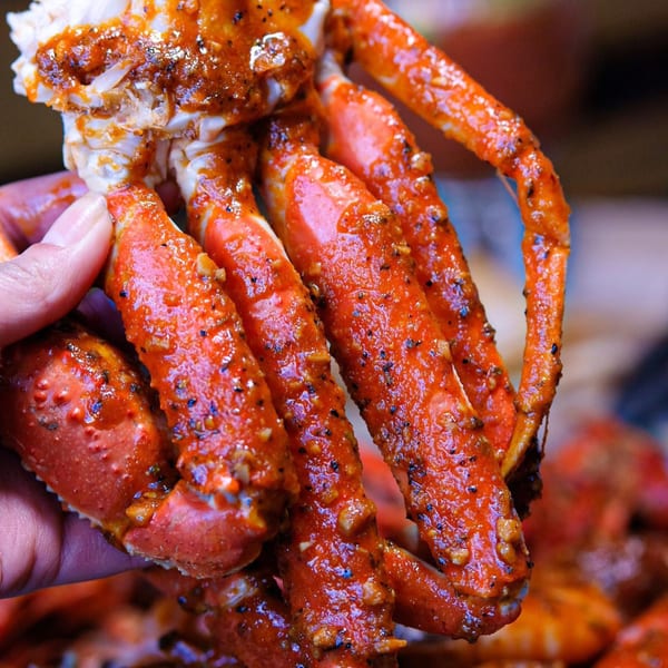 A hand holds up a cluster of bright red, seasoned crab legs from The Crab Station.